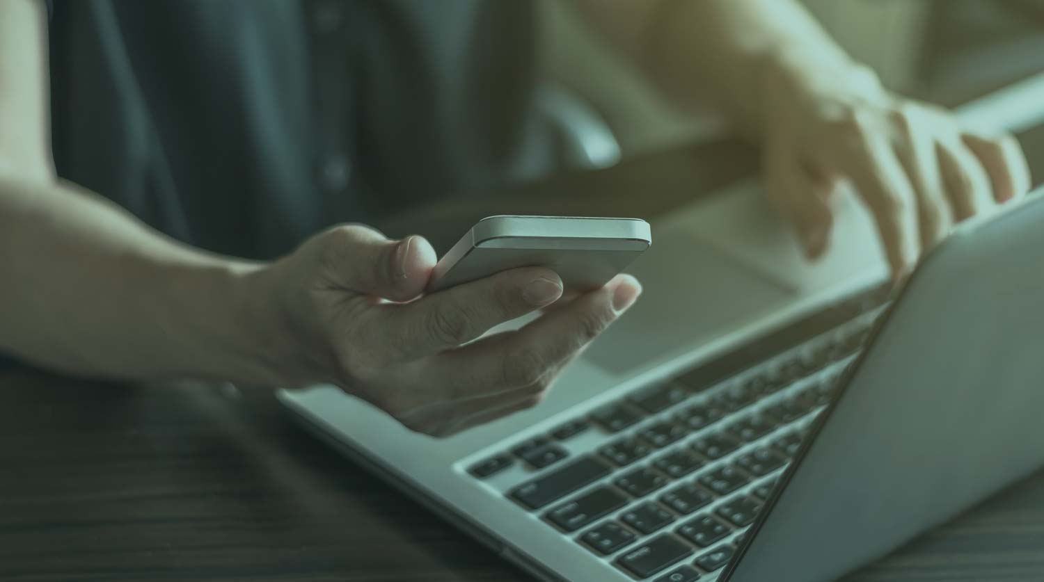 Closeup of hand searching for CV structure examples on mobile phone and laptop.